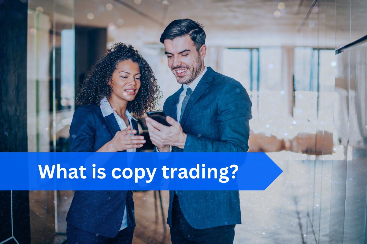 Two professionally dressed individuals in a modern office setting, smiling while looking at a smartphone. A blue banner with white text reads 'What is copy trading?